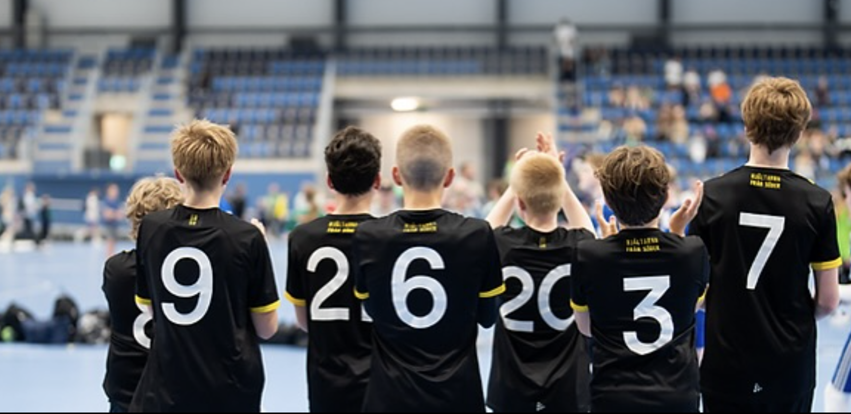 Ungdomslag i svarta matchtröjor står tillsammans i en idrottshall